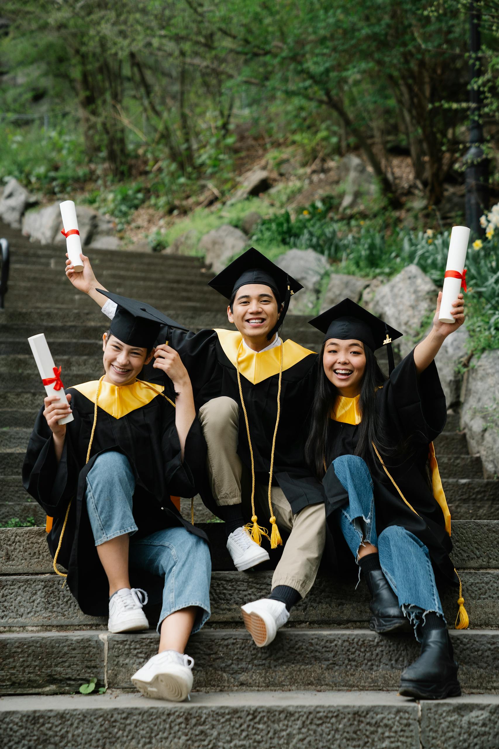 Group of graduates in gowns celebrating with diplomas on outdoor steps.